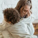 a child is hugging her tired and frustrated mother